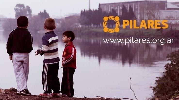 An image of three children standing by a river on an overcast day, with the Pilares logo and web address included in the image. 